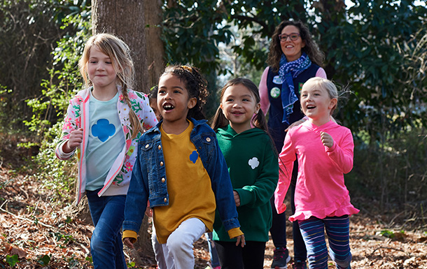 group of young girl scout daisies hiking with adult volunteer