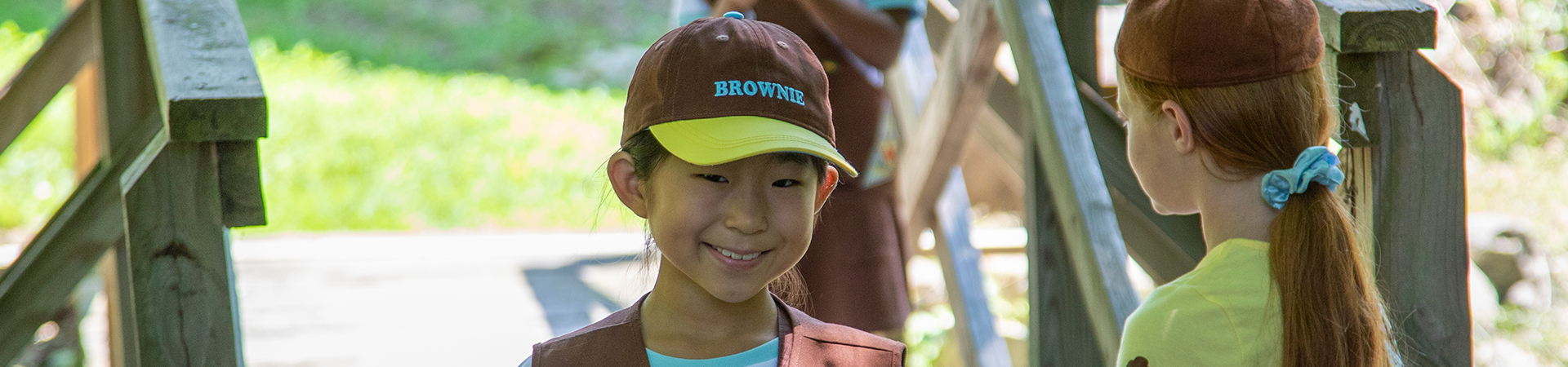  group of junior girl scouts walking outside hugging smiling at camera in junior vest and sash with badges 